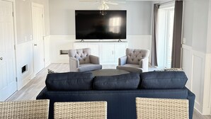 Ein modernes Wohnzimmer mit einem dunkelblauen Sofa, zwei Sesseln, einem Flachbildfernseher und einem Deckenventilator.