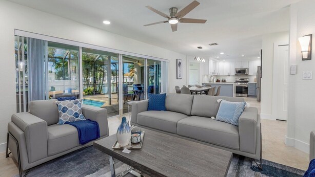A modern living room with a grey sofa, a coffee table, and a pool view through large glass doors. - Water's Edge-Intracoastal Gem with Pool and Spa (Saint Petersburg)