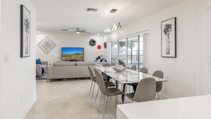 A modern living room with a TV, sofa, and dining area with chairs and a table. - Water's Edge-Intracoastal Gem with Pool and Spa (Saint Petersburg)