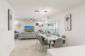A modern living room with a TV, sofa, and dining area with chairs and a table. - Water's Edge-Intracoastal Gem with Pool and Spa (Saint Petersburg)