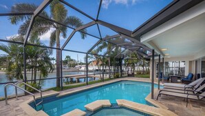 An indoor swimming pool with a glass ceiling, lounge chairs, and a view of palm trees and water. - Water's Edge-Intracoastal Gem with Pool and Spa (Saint Petersburg)