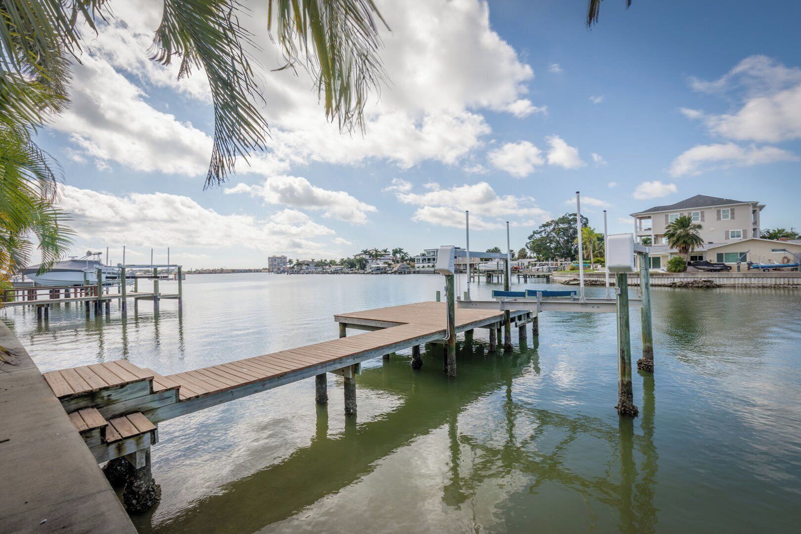 A waterfront dock with a wooden pier extending into calm water, surrounded by residential buildings and palm trees.