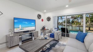 A modern living room with a flat-screen TV, a fireplace, a pool view, and a ceiling fan. - Water's Edge-Intracoastal Gem with Pool and Spa (Saint Petersburg)