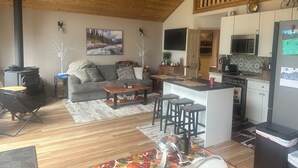 Un saló d'estar acollidor amb una llar de foc, un sofà, una taula de centre i una zona de cuina amb microones i nevera.