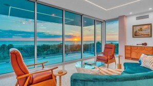 A modern living room with large glass windows, a sofa, a chair, and a small table. - Casa Floridita by Duncan Real Estate (Anna Maria)