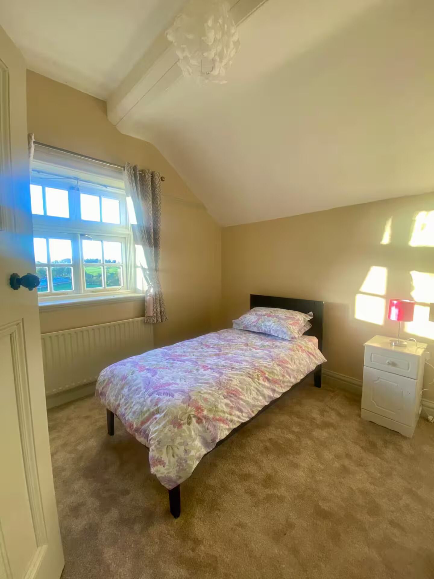 Een slaapkamer met een bed, nachtkastje, raam met gordijnen en een radiator.
