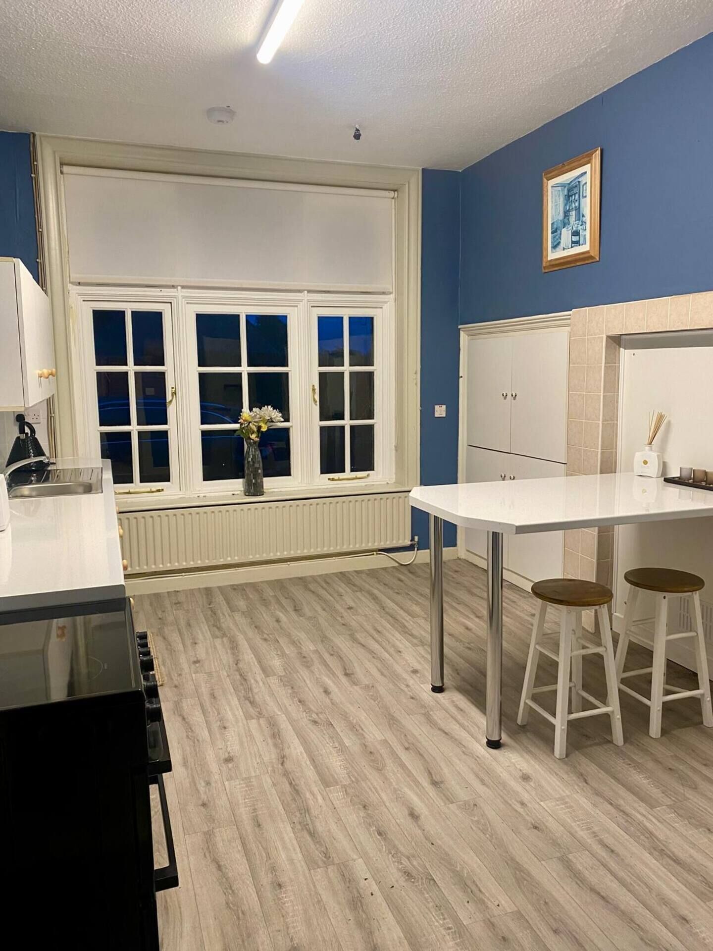 Una cucina moderna con un piano di lavoro bianco, due sgabelli, una finestra con persiane e un termosifone.