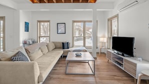 Una sala de estar moderna con sofá, mesa de centro, televisor y ventanas amplias.