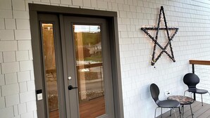 Una puerta con el número '30' encima, una decoración de luz con forma de estrella en la pared y dos sillas en una terraza de madera.