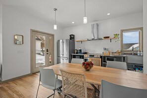 A modern kitchen with stainless steel appliances, a wooden dining table, and a view of the outdoors. - 3BR New Modern Westerly Home – Walk to Downtown (Westerly)