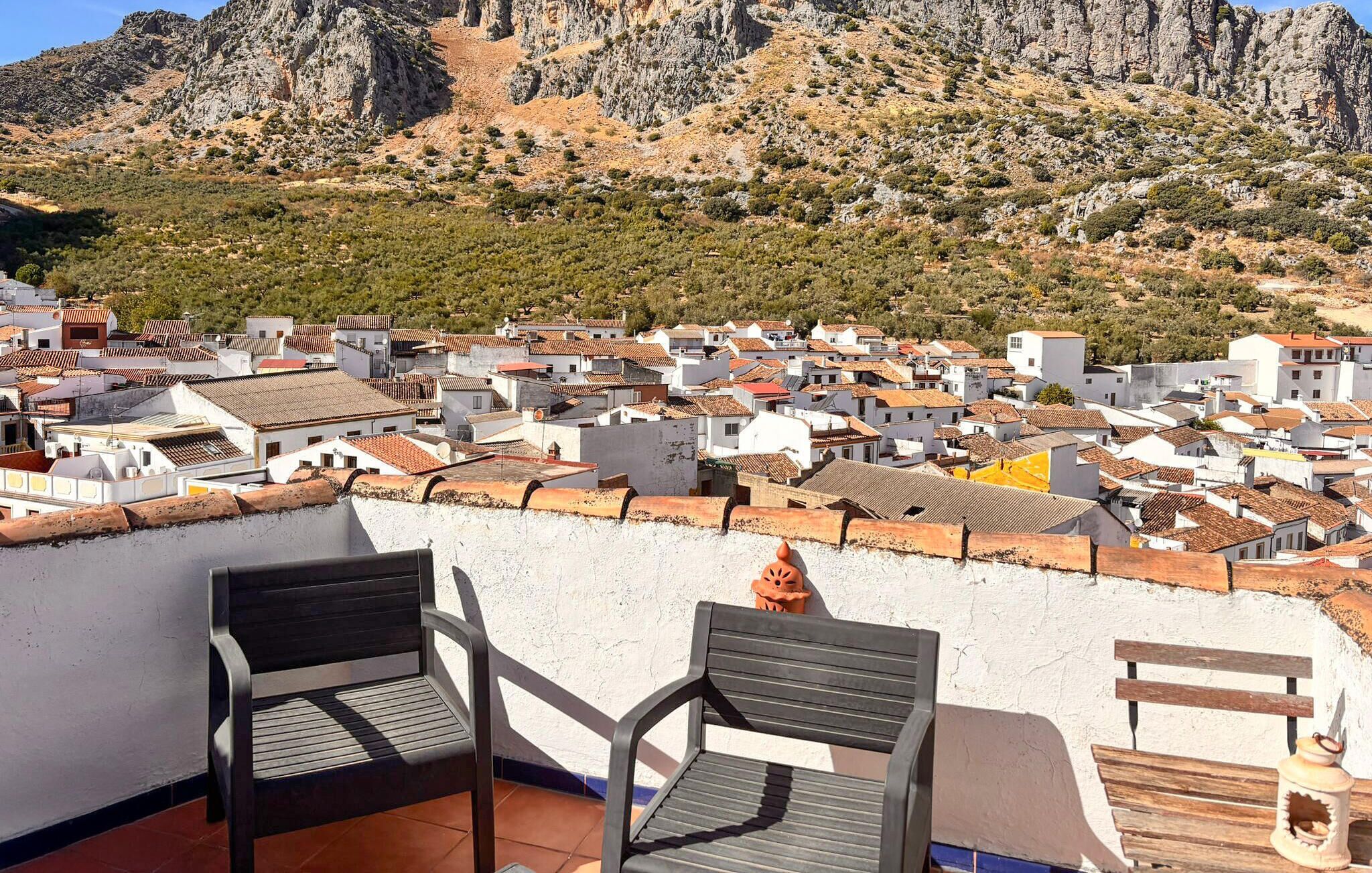 Una terraza con dos sillas y una mesa, con vista a un pueblo de edificios con tejados de teja y montañas al fondo.