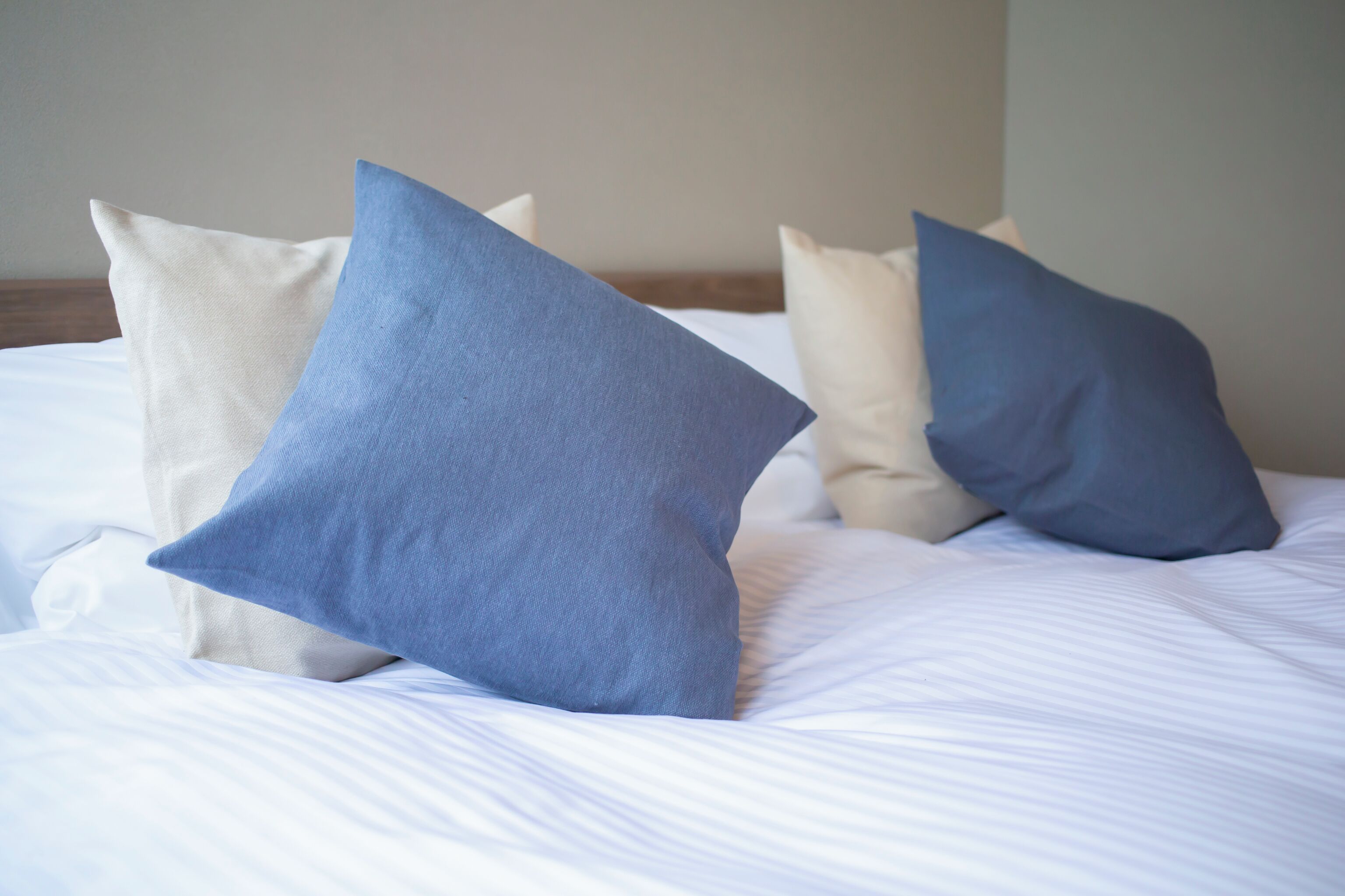 Ein Bett mit weißer Bettwäsche und drei Kissen, davon zwei blau und eines beige.