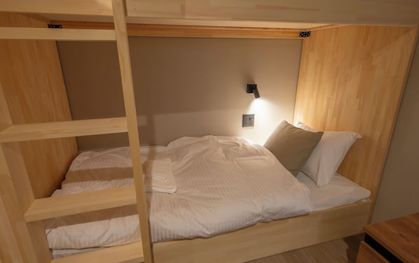 Un lit superposé avec une structure en bois, une lampe fixée au mur et une table de chevet.