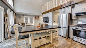 A modern kitchen with a dining area, stainless steel appliances, and a loft bedroom with a wooden staircase. - White Mtns Holiday Home! Cabin 1 Mi to Skiing (Campton)