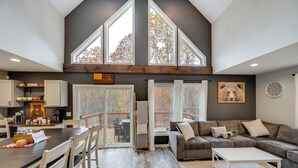 A spacious living area with a large window, a cozy seating area, and a kitchen with modern appliances. - White Mtns Holiday Home! Cabin 1 Mi to Skiing (Campton)