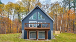 A blue cabin with a wooden deck and large windows, surrounded by autumn trees. - White Mtns Holiday Home! Cabin 1 Mi to Skiing (Campton)