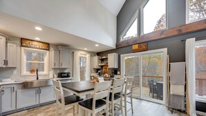 A modern kitchen with white cabinetry, a dark countertop, and a dining area with white chairs. - White Mtns Holiday Home! Cabin 1 Mi to Skiing (Campton)
