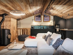 Un espacio habitable moderno tipo loft con techo de madera, cocina con armarios oscuros y un sofá blanco con cojines estampados.