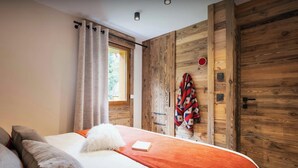 Ein Schlafzimmer mit Bett, Kissen, Decke, Holzwänden, einem Fenster und einer Tür.