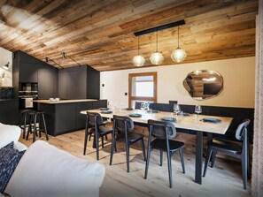 Une cuisine moderne avec des meubles de couleur sombre, une table à manger en bois pour six personnes et un grand miroir au mur.