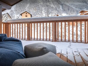 En træterrasse med sneklædte gelændere, en ternet skammel og udsigt til sneklædte træer og bygninger i baggrunden.
