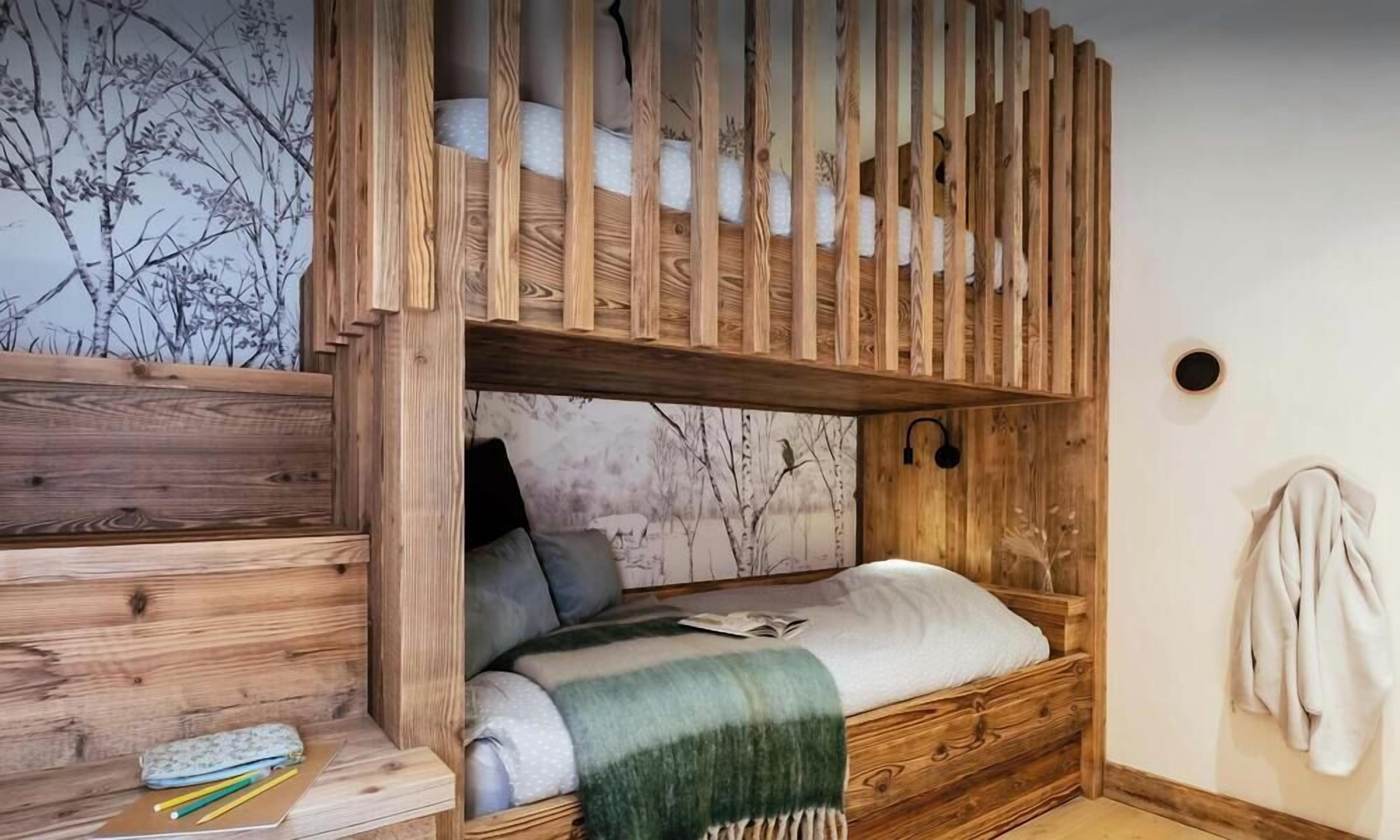 A wooden bunk bed with a built-in desk and shelving, a wall-mounted lamp, and a cozy blanket.