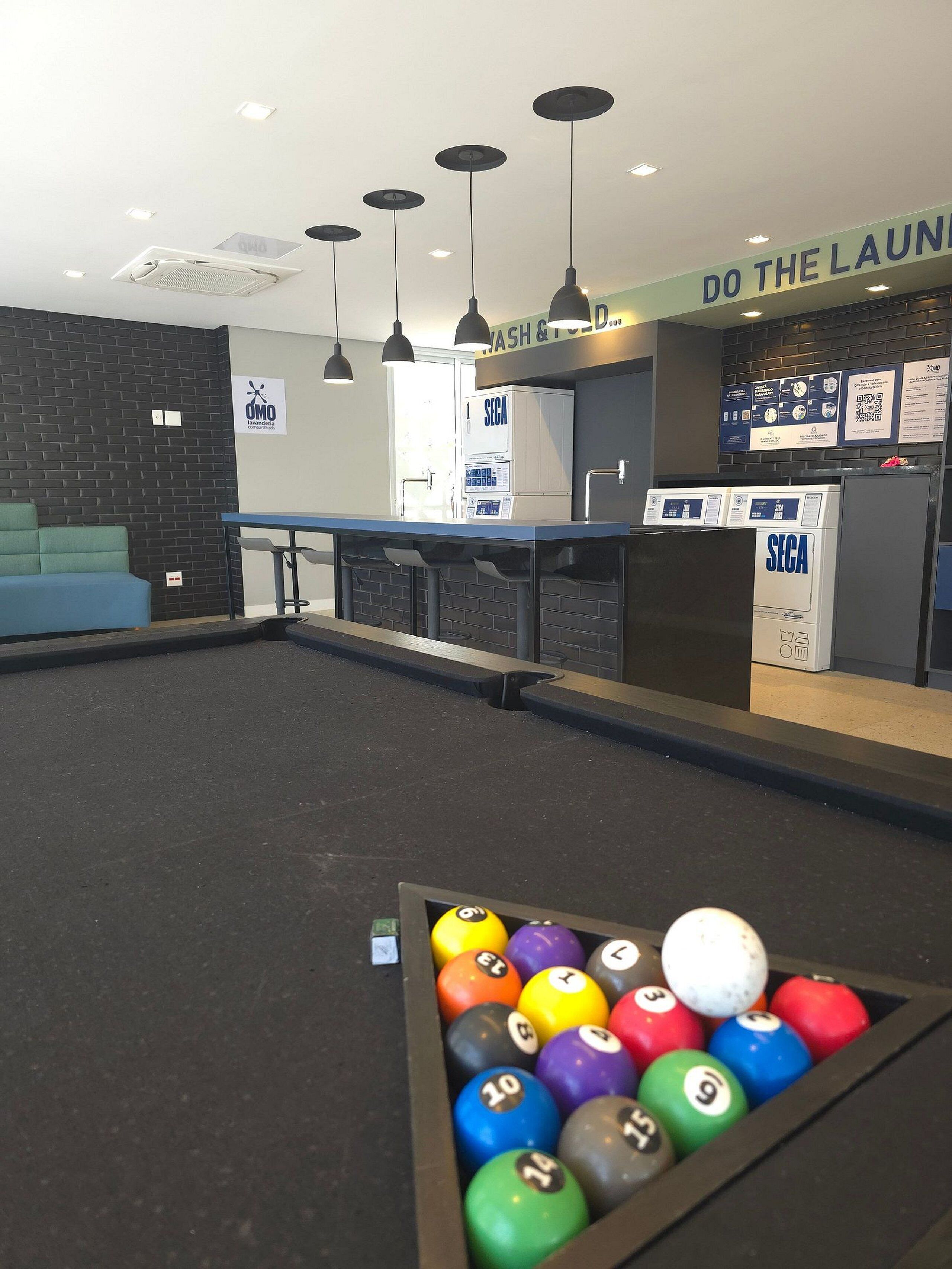 A pool table with a ball rack, a sofa, a wash station, and a sign that says 'DO THE LAUNDRY'.