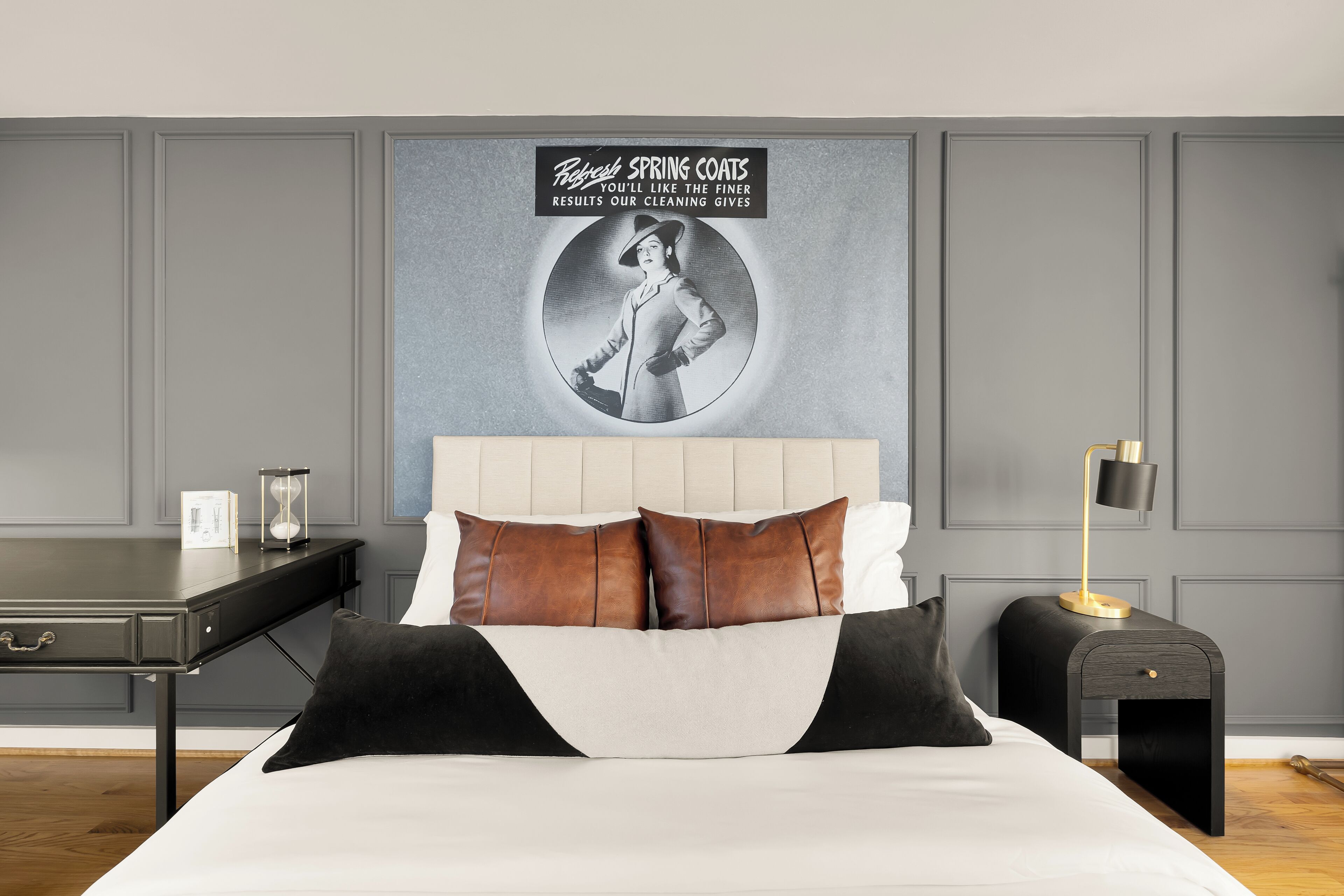 Une chambre à coucher avec un lit, des oreillers, une table de chevet, une lampe et un mur orné d’un tableau et d’un texte.