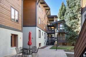 A courtyard with a table and chairs, a red umbrella, and a staircase leading to an upper level. - Vail Condo - Pet Friendly & Steps to Ski Lift (Vail)