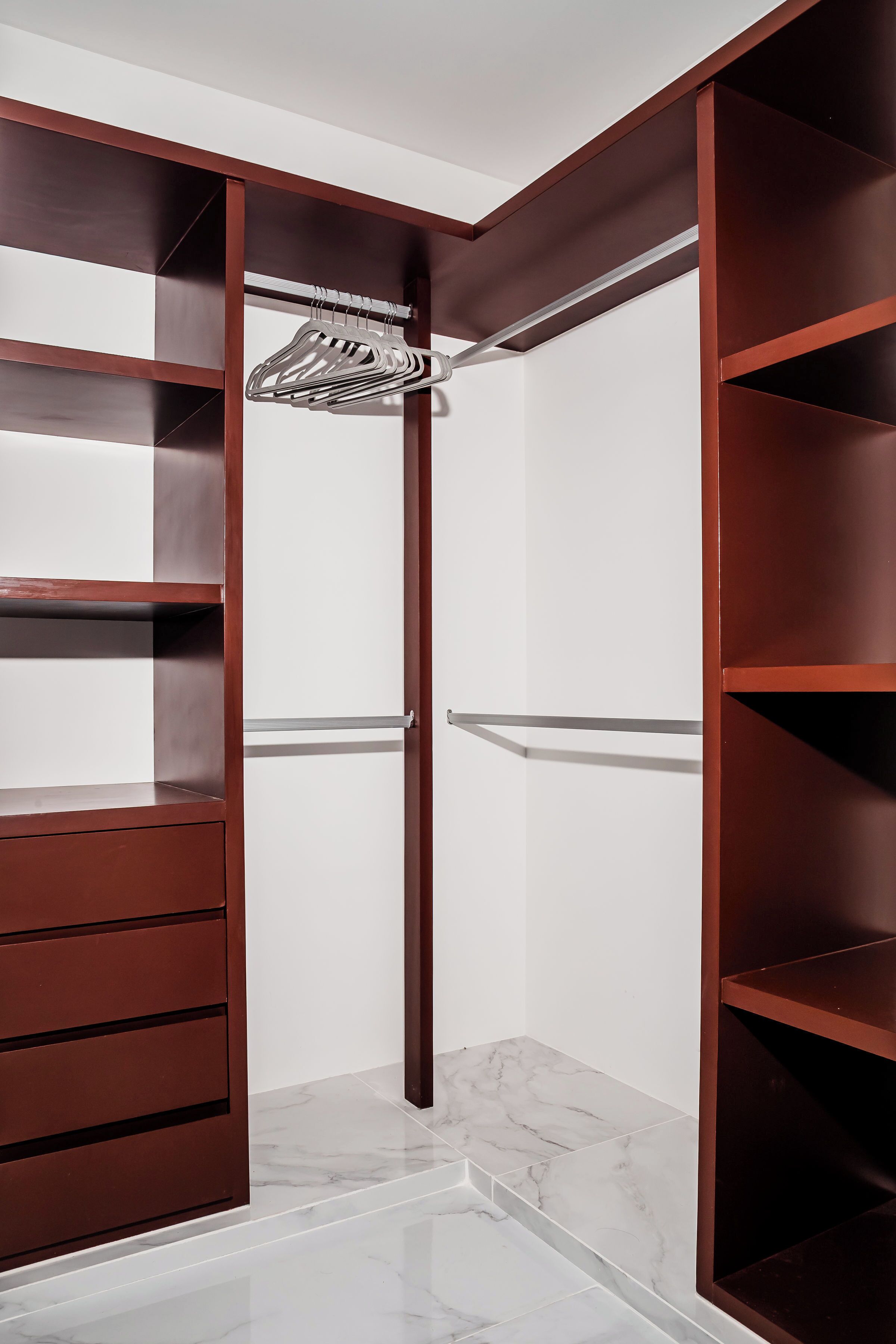 Um closet espaçoso com várias prateleiras e gavetas, um cabideiro e piso de mármore.
