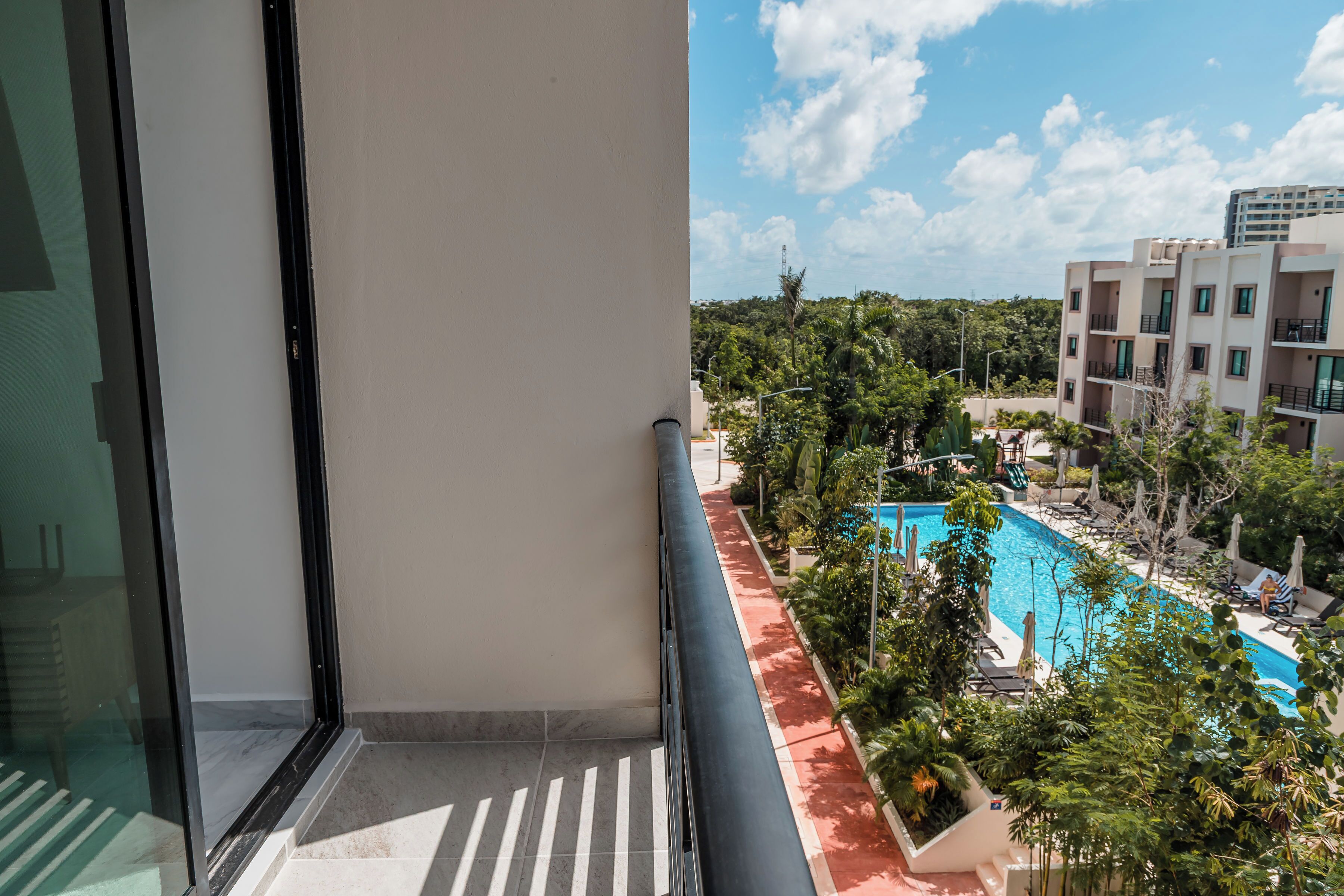 Ein Balkon mit freiem Blick auf ein Schwimmbecken, üppiges Grün und ein modernes Gebäude im Hintergrund.