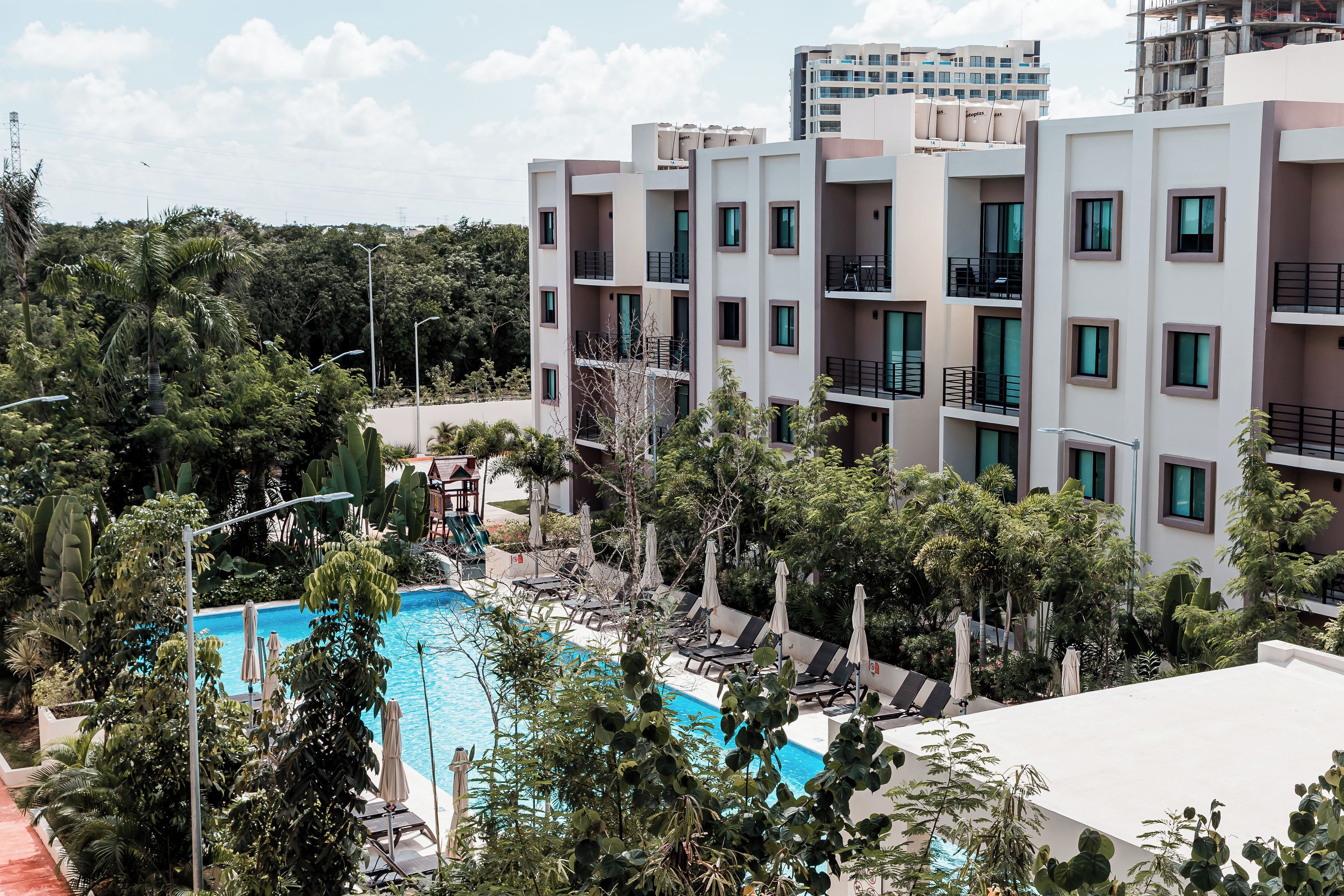 A modern hotel with a swimming pool surrounded by lush greenery and multiple balconies.