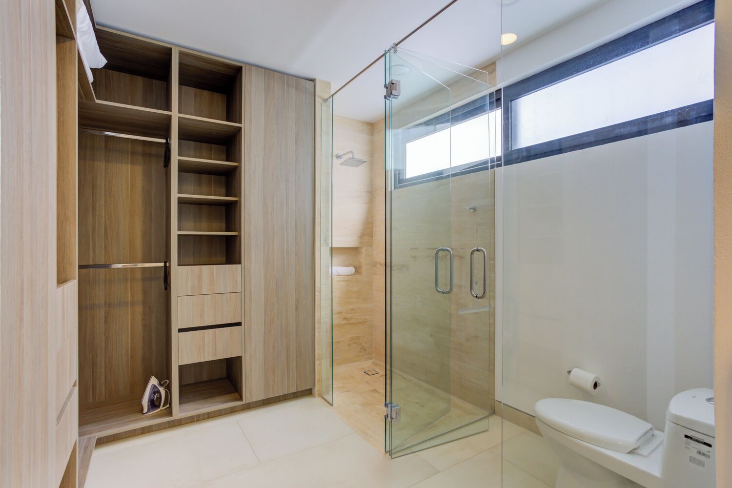 A modern bathroom with a walk-in shower, a toilet, and a built-in wardrobe with multiple shelves.