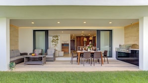 A modern outdoor dining area with a table set for four, surrounded by wicker furniture and a grassy lawn. - Vista Natura-Luxury Home Near the Beach (Nuevo Nayarit)