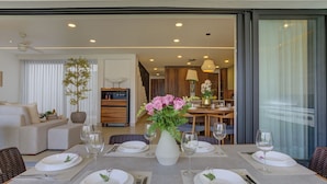 A dining area with a table set for four, a vase of flowers, and a view of the living room and kitchen in the background. - Vista Natura-Luxury Home Near the Beach (Nuevo Nayarit)