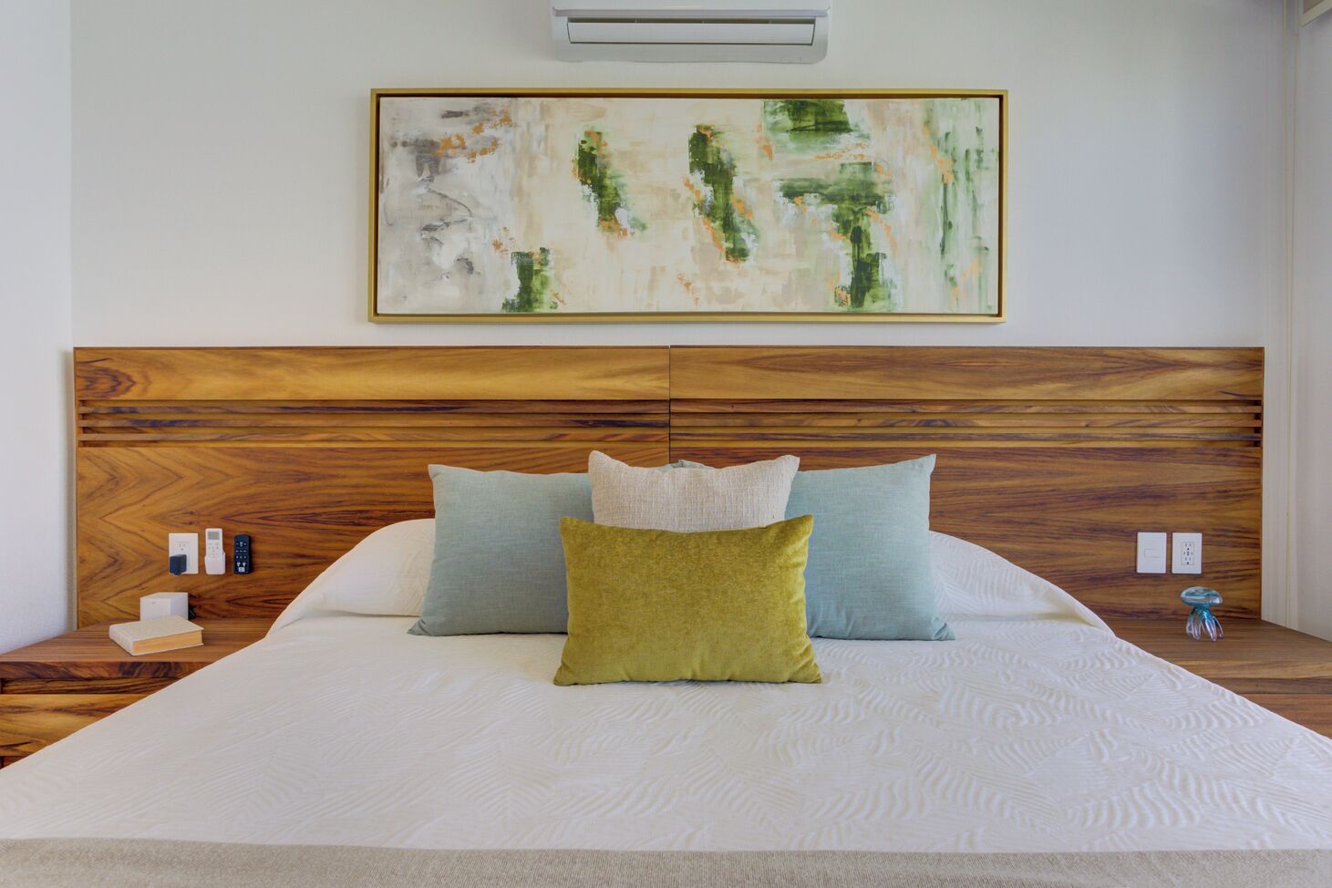 A bedroom with a wooden headboard, a white bedspread, and three pillows in different colors.