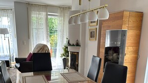 Ruokailutilassa on lasipöytä, mustat tuolit ja kuviollinen pöytäliina. Siellä on myös sohva, jossa on päällä heittopeitto, sekä takka, jonka yläpuolella on koristeellinen takanreunus.
