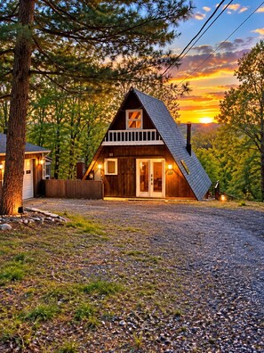 A cabin with a sloped roof, a front porch, and a gravel driveway.