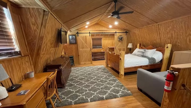 Une chambre confortable, décorée dans un style chaleureux avec du bois, comprenant un lit, un bureau et une chaise, une petite table et un extincteur.