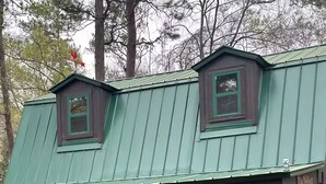 Une cabane rustique avec un toit en métal vert, une véranda en bois et un drapeau de l’État du Texas.