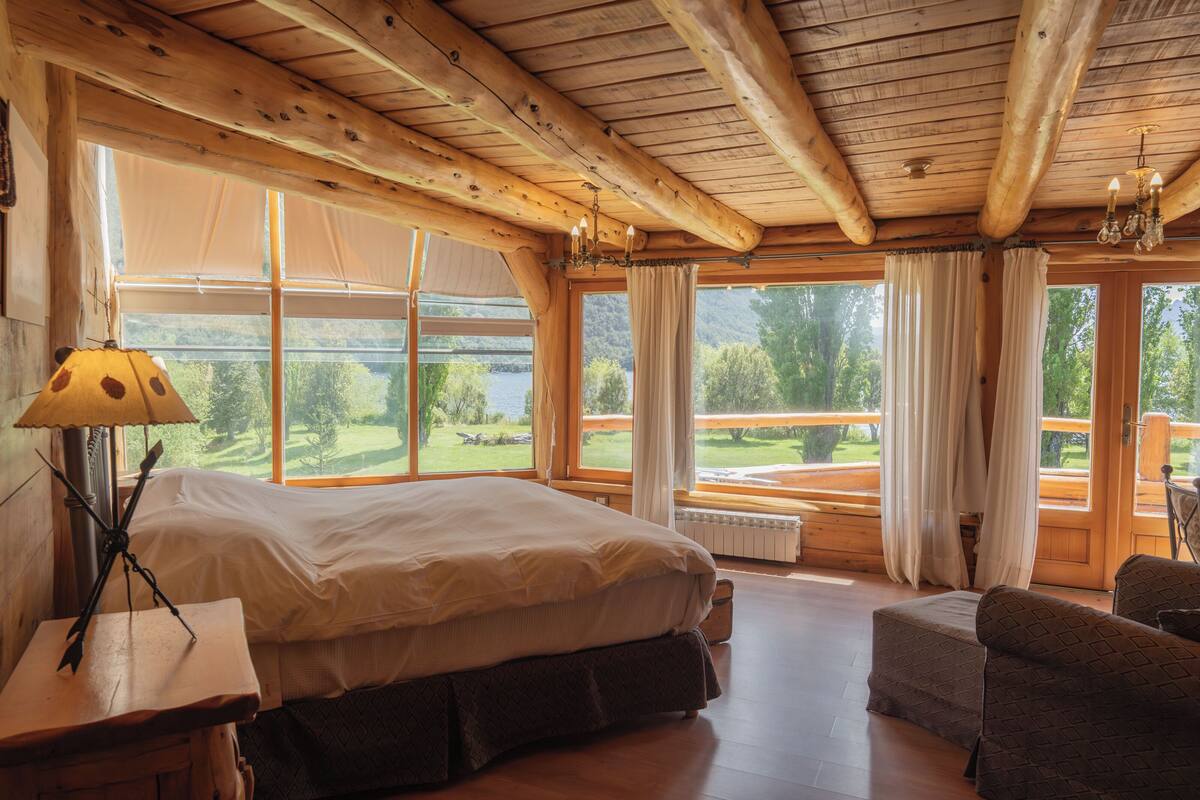 A wooden cabin bedroom with a large bed, a small sofa, and a view of a lake.