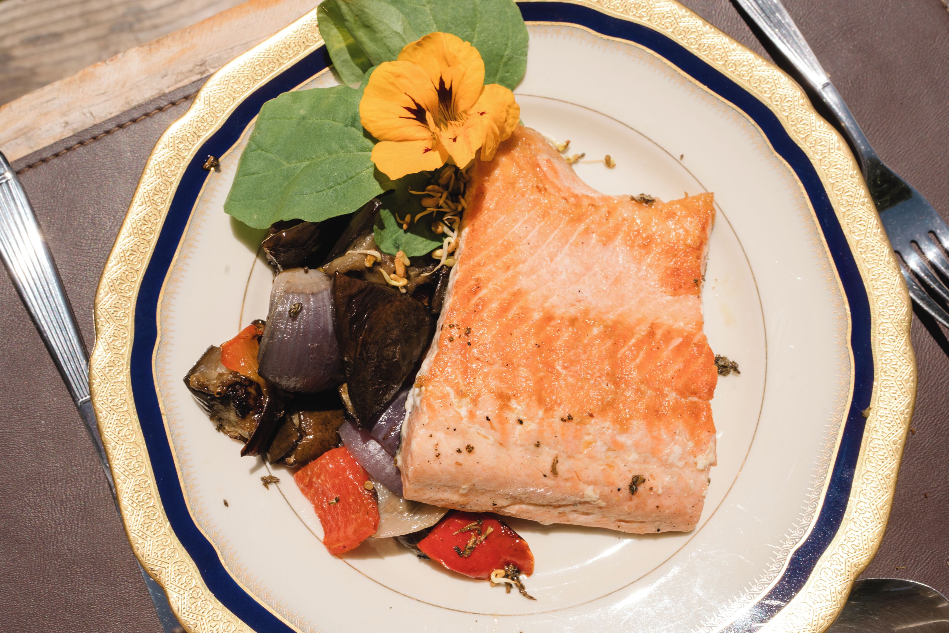 A plate with salmon, vegetables, and a flower.