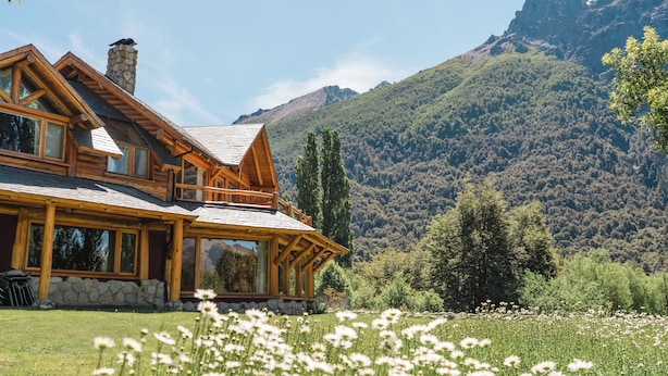 Une cabane en rondins avec une cheminée en pierre, de grandes fenêtres et une vue sur un paysage montagneux.