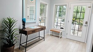 Quarto com escrivaninha de madeira, um banco, um espelho grande e uma porta com vista.