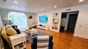 Sala de estar com sofá, poltrona, televisão, estante de livros e piso de madeira.