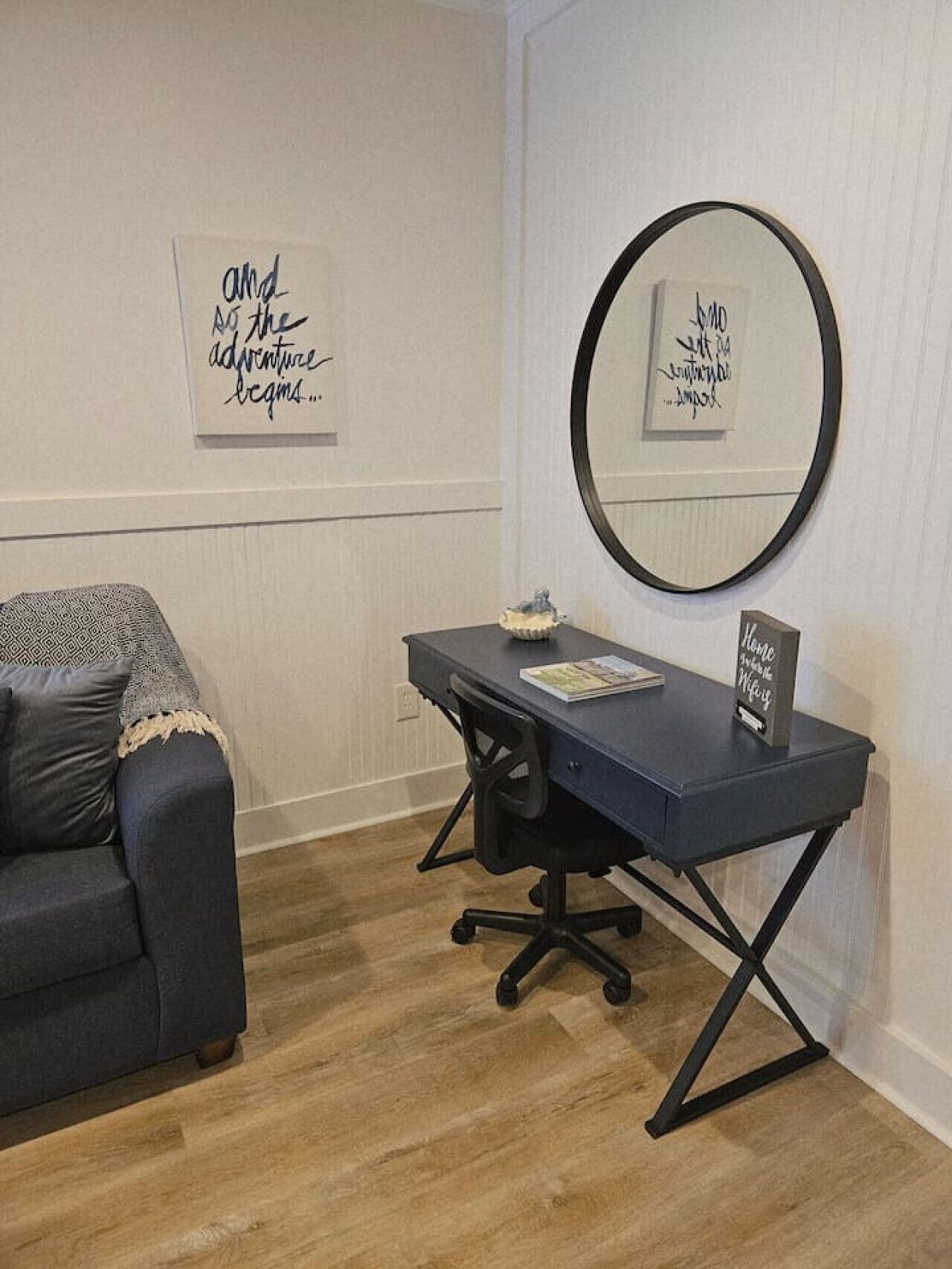 A room with a desk, a chair, a couch, and two framed motivational quotes on the wall.