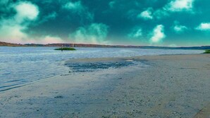 Ein Strand mit einer kleinen Insel, ruhigem Wasser und bewölktem Himmel.