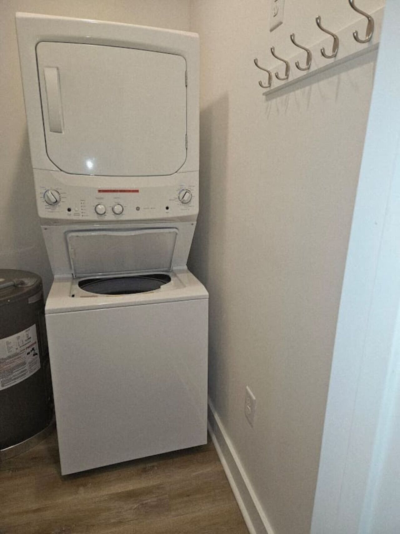 A compact washer and dryer unit in a small laundry room with a wooden floor and a wall-mounted drying rack.