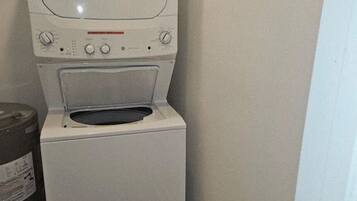 A compact washer and dryer unit in a small laundry room with a wooden floor and a wall-mounted drying rack.