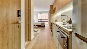 A modern kitchen with stainless steel appliances, a wooden door, and a view of a bedroom with a bed and a window. - Haus by Wynwood House (Bogotá)